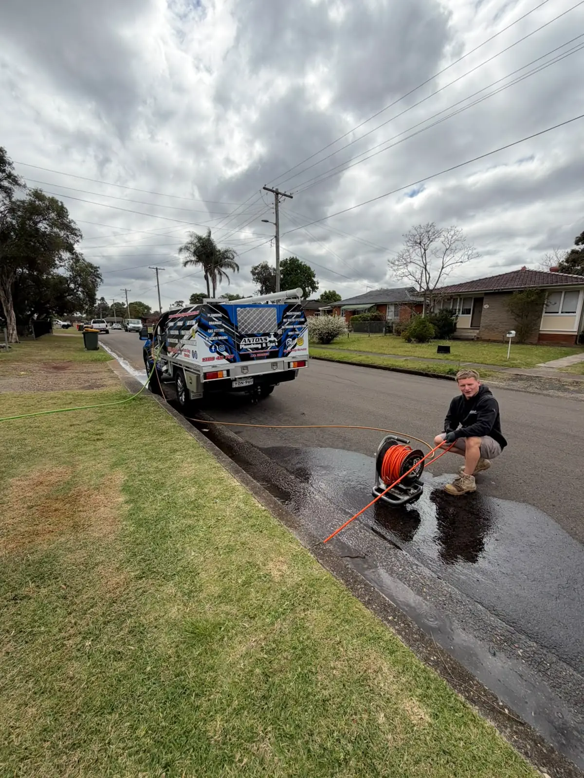Plumber operating drain-clearing equipment beside an Antons vehicle