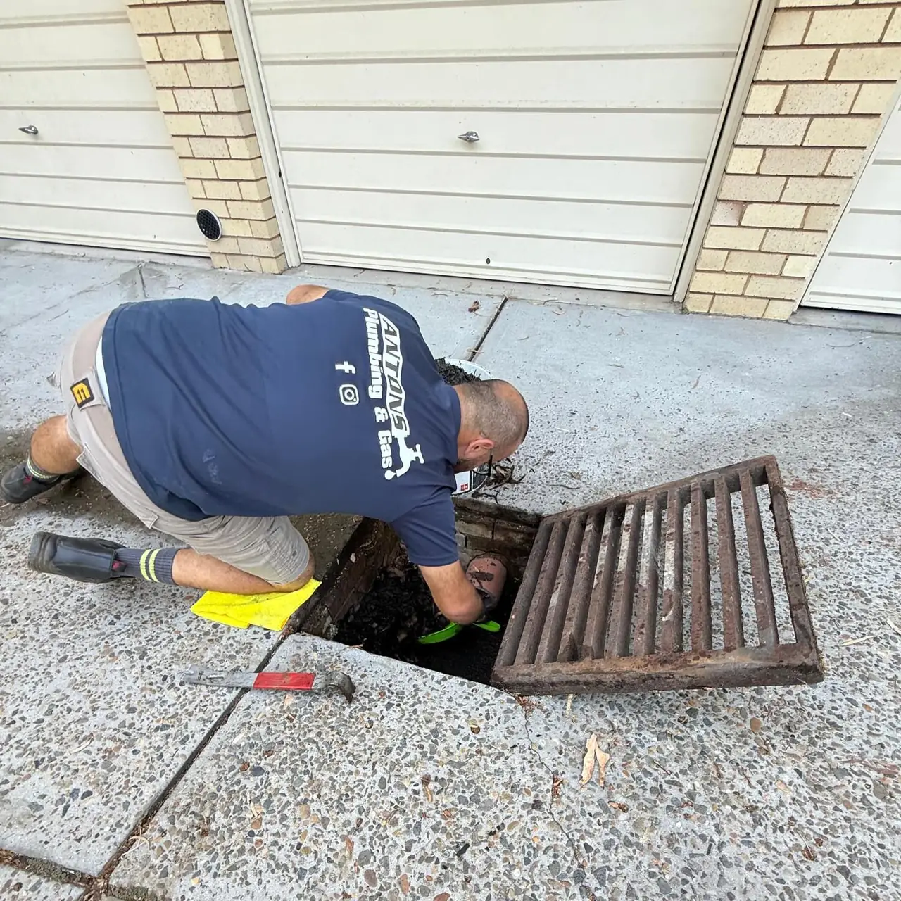 Antons plumber inspecting pipework through an outdoor drainage opening