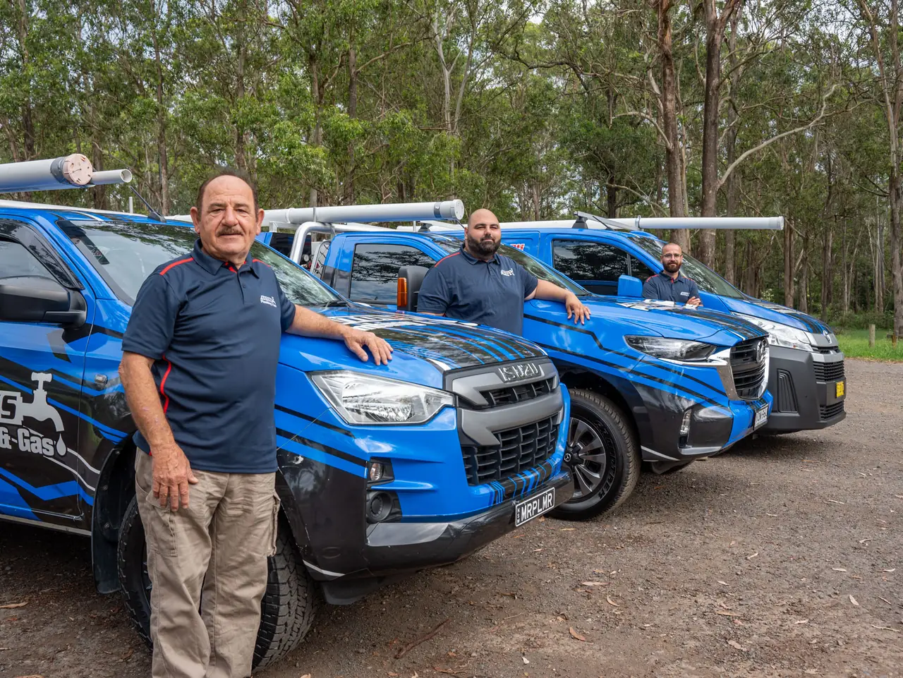 Three Antons plumbers standing beside blue plumbing vehicles