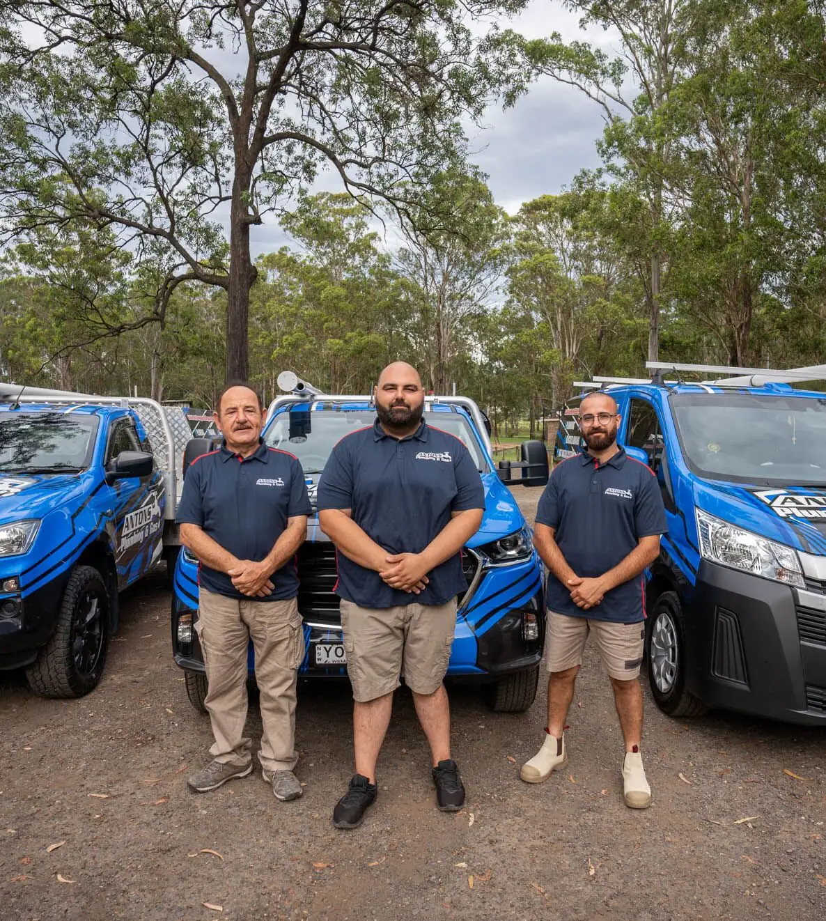 Antons plumbing team standing with blue service vehicles