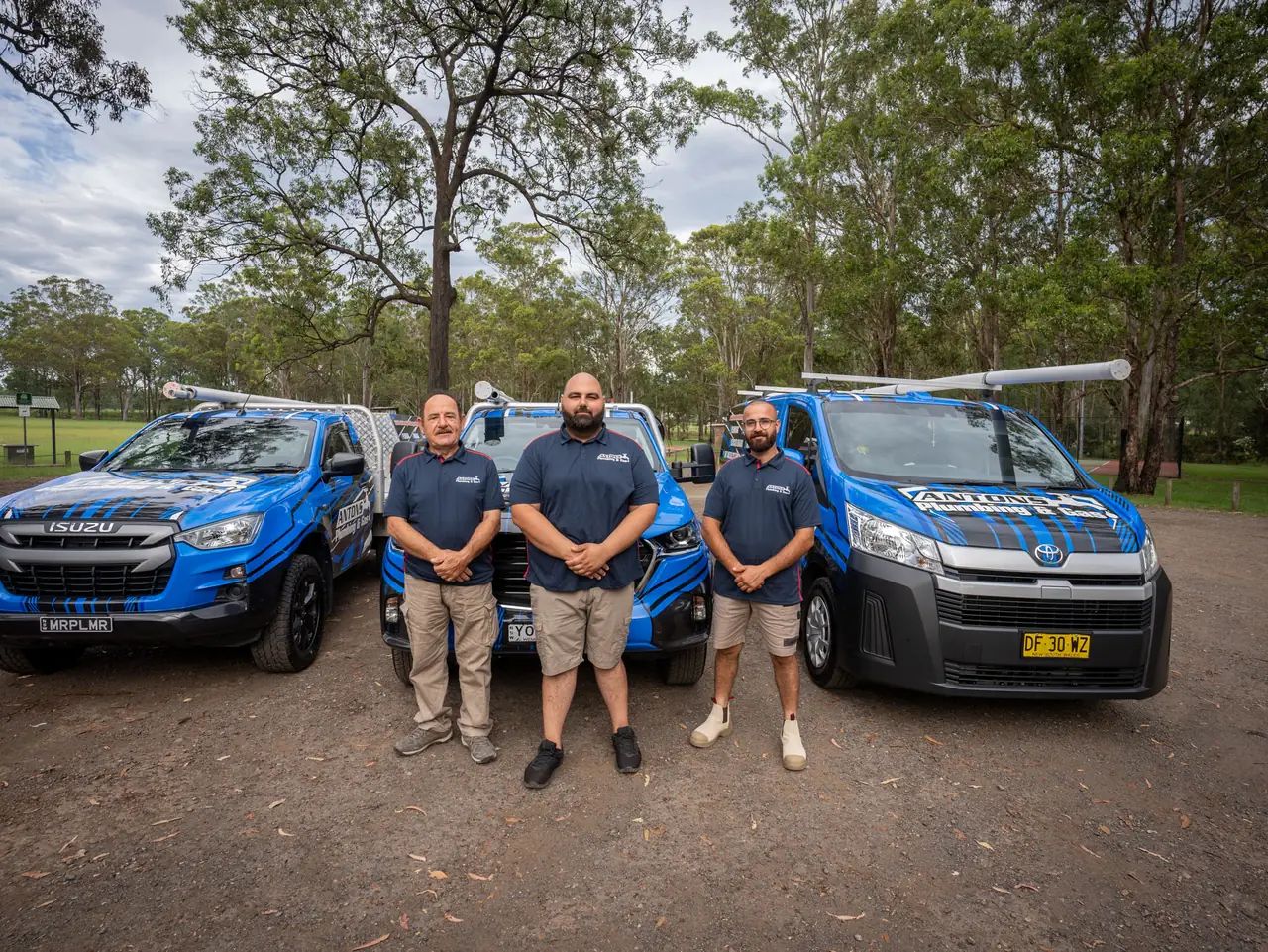 Three Antons plumbers standing between blue service vehicles