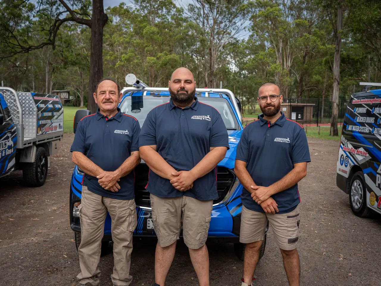 Three Antons plumbers standing in front of a blue service vehicle